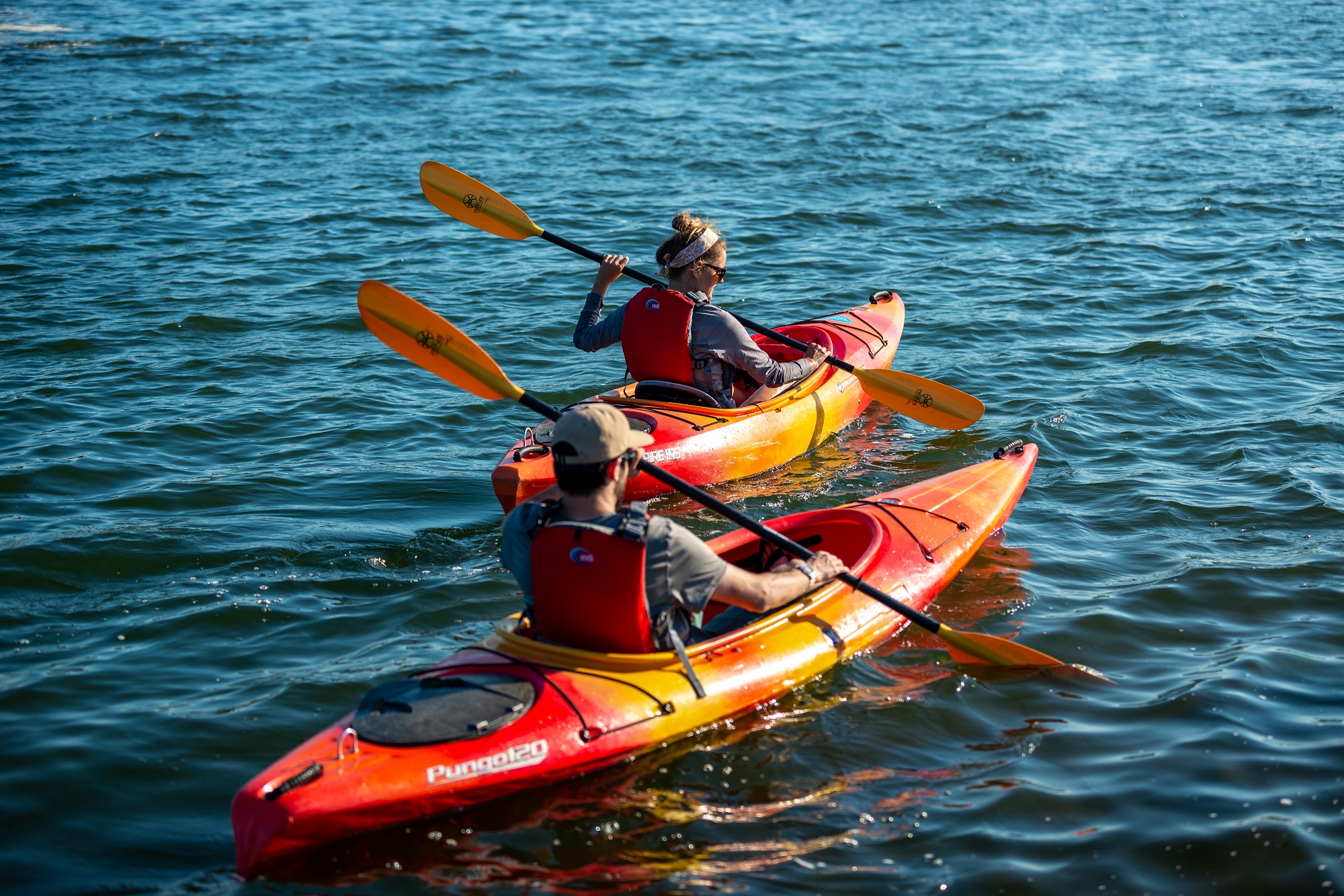 Two people paddling kayaks with neutral feathered paddles 